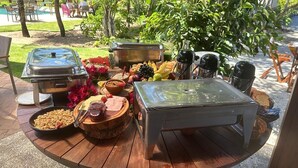 A buffet setup with various food items and condiments on a wooden table outdoors.