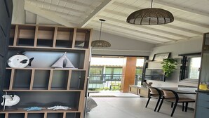 A spacious living area with a high ceiling, wooden shelves, and a dining area with chairs and a table.