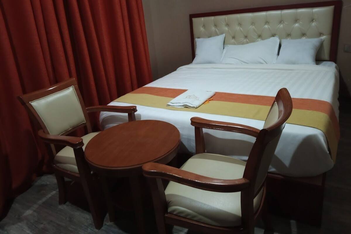 Camera d'albergo con un letto, due sedie di legno, un tavolino rotondo e una tenda rossa.