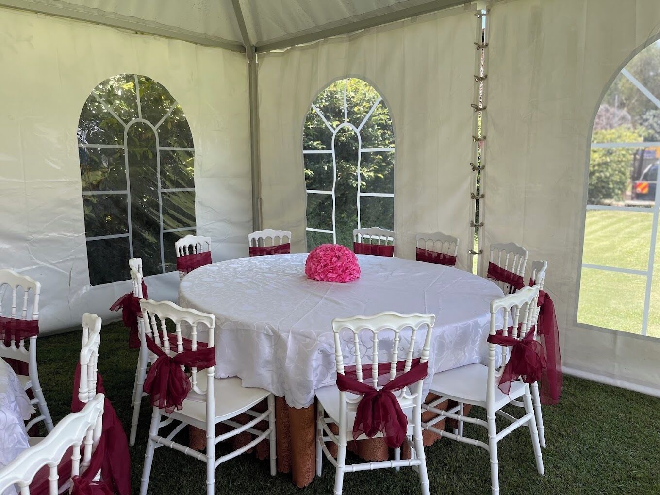 A tented dining area with round tables and white chairs, each with red sashes.