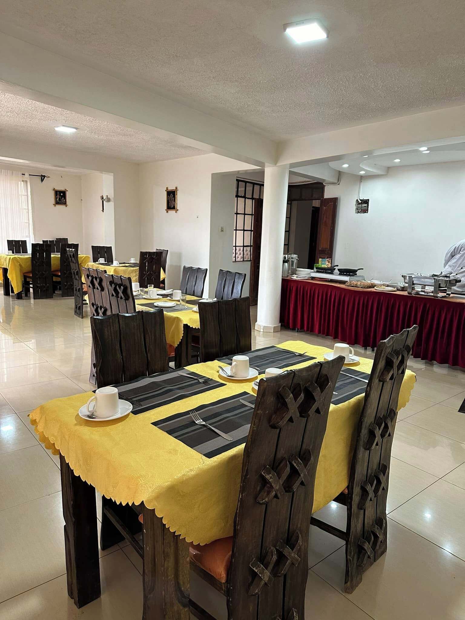 A dining area with tables set for meals, chairs, and a buffet counter in the background.