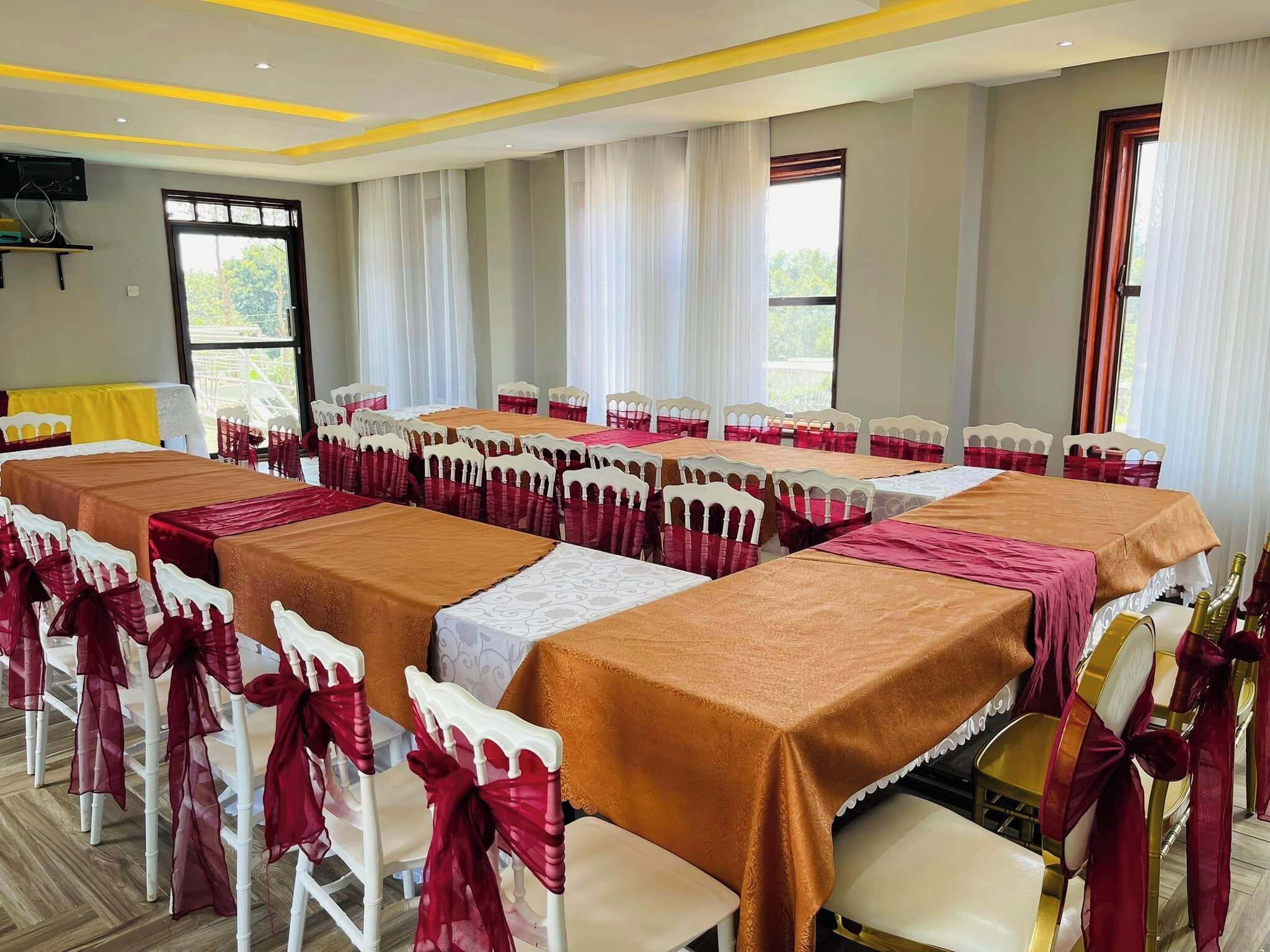 A banquet hall with multiple tables, each covered with a brown tablecloth and surrounded by chairs with red sashes.