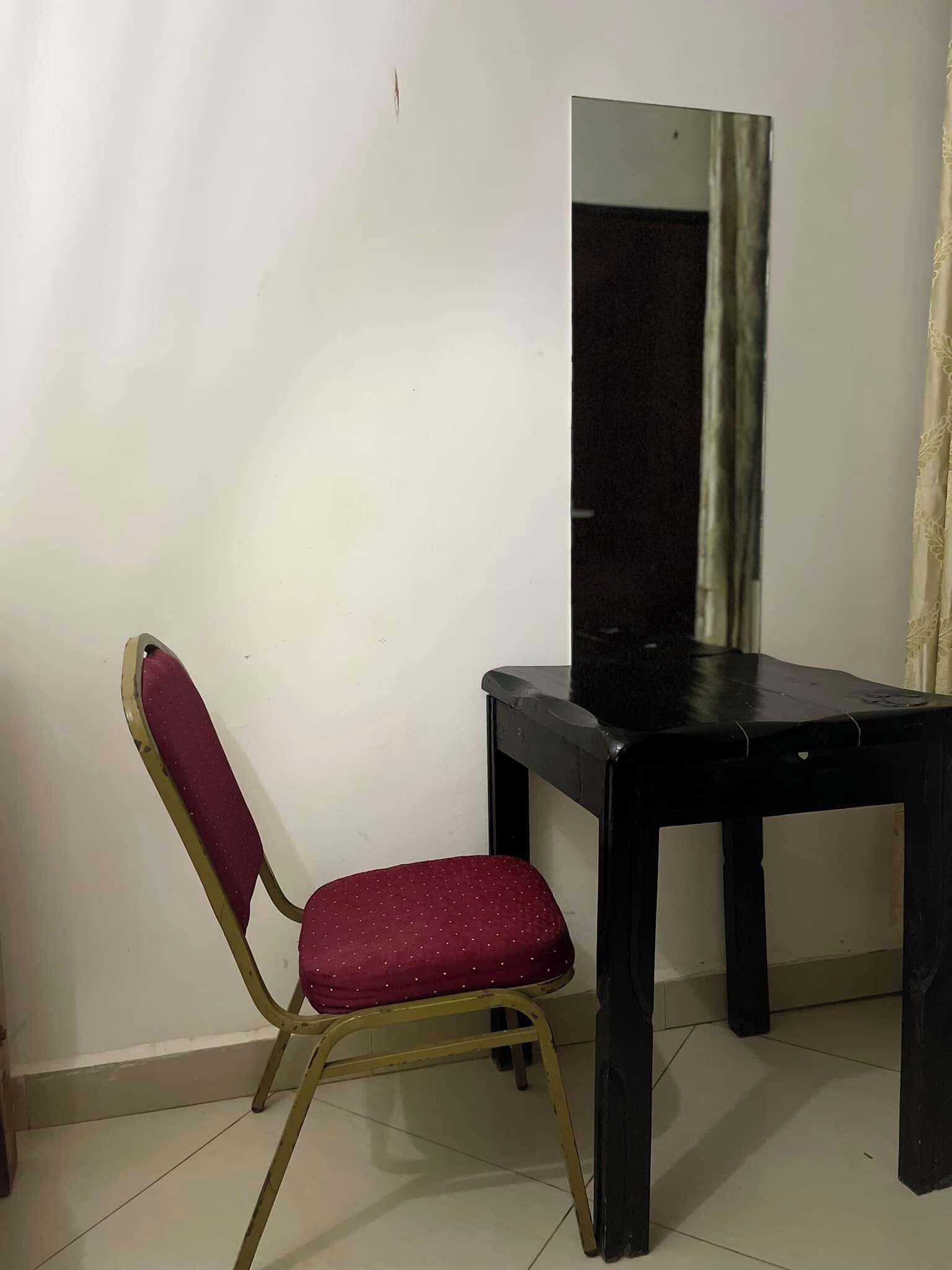A small room with a single chair and a table, a mirror on the wall, and a curtain partially drawn.