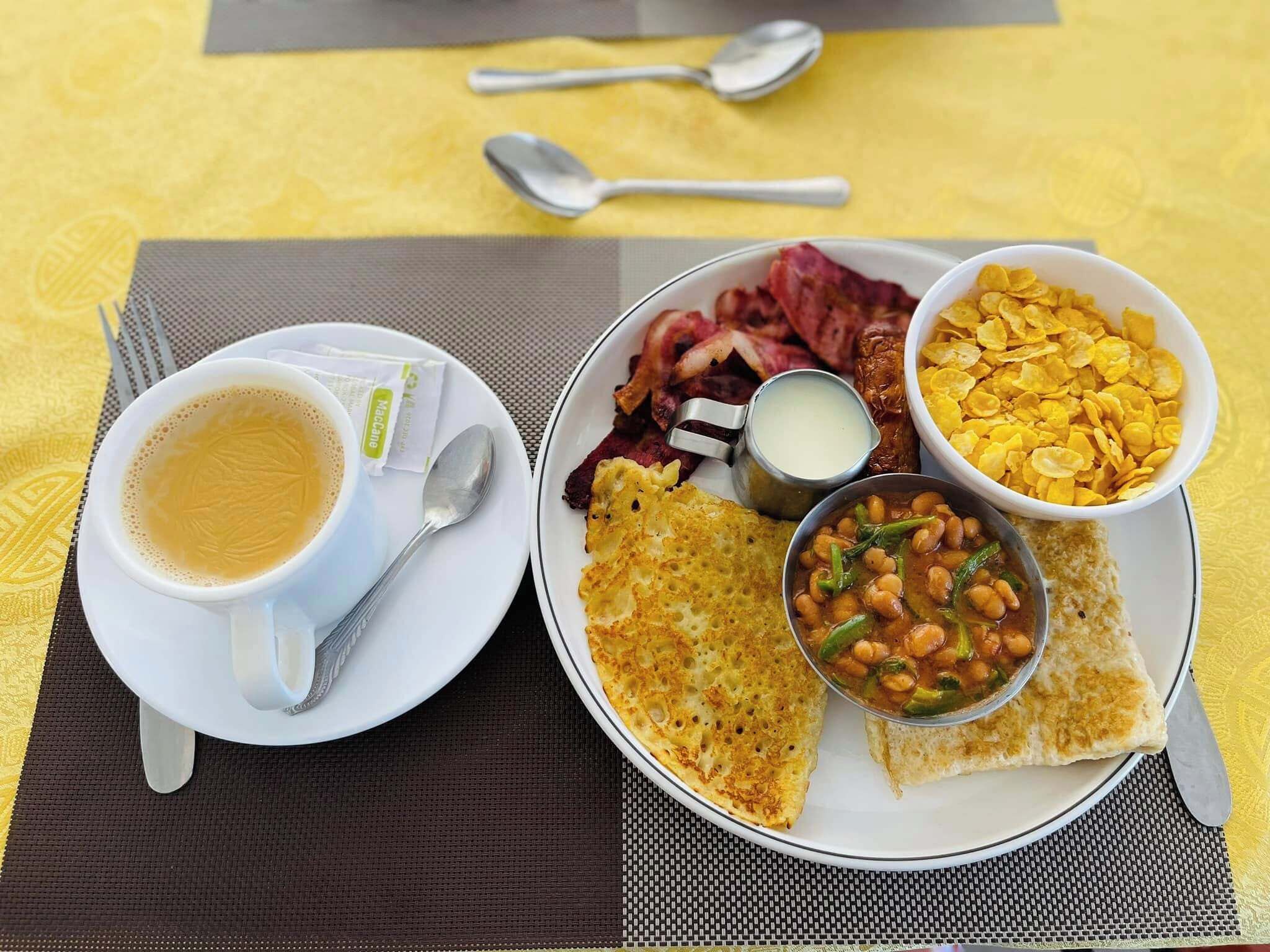 A breakfast plate with coffee, bacon, beans, and cornflakes.