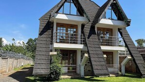 Uma casa de dois andares com telhado inclinado, janelas amplas e uma varanda.