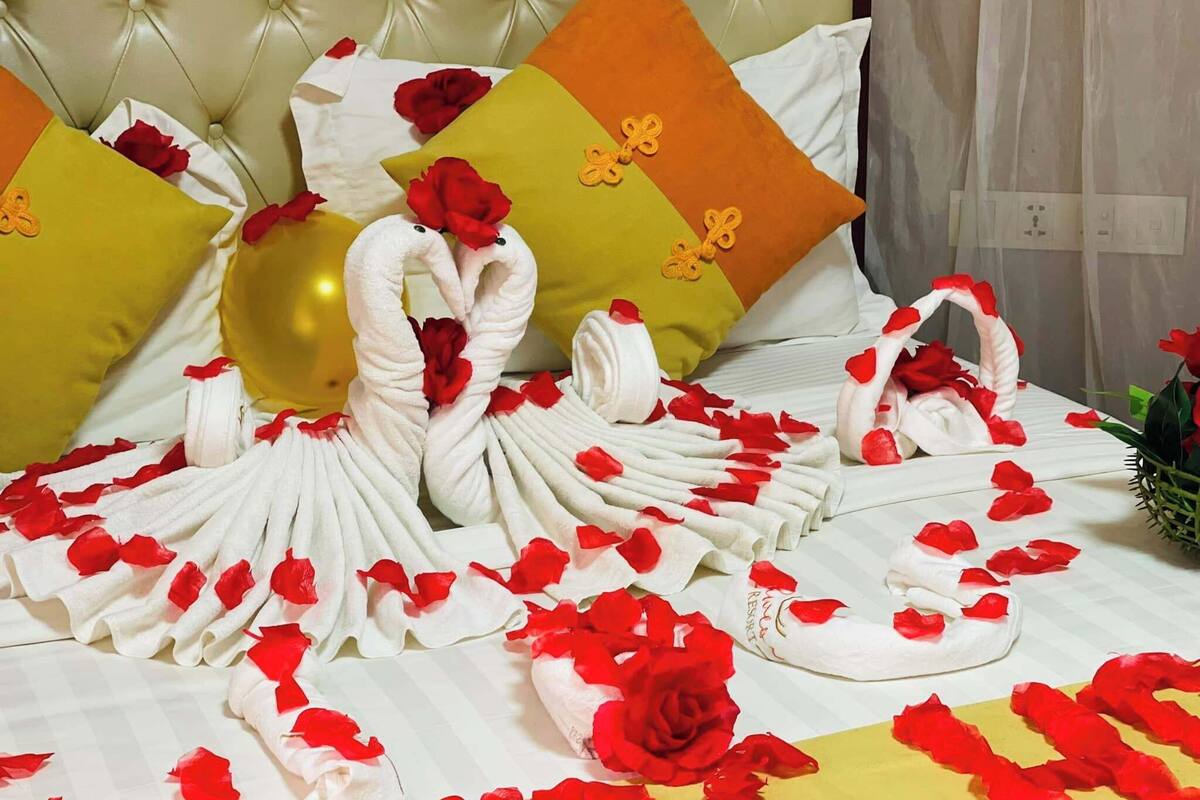 Un letto decorato con petali di rosa e cigni realizzati con asciugamani, cuscini e un vaso con una rosa.