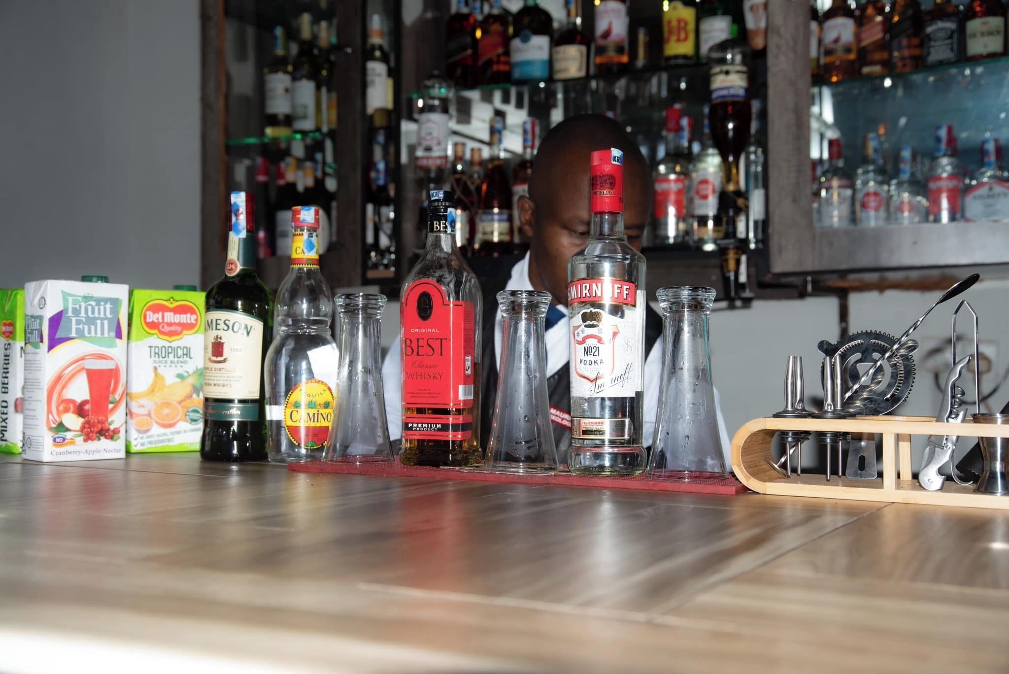 A bar counter with various bottles of alcohol and a juice cooler.
