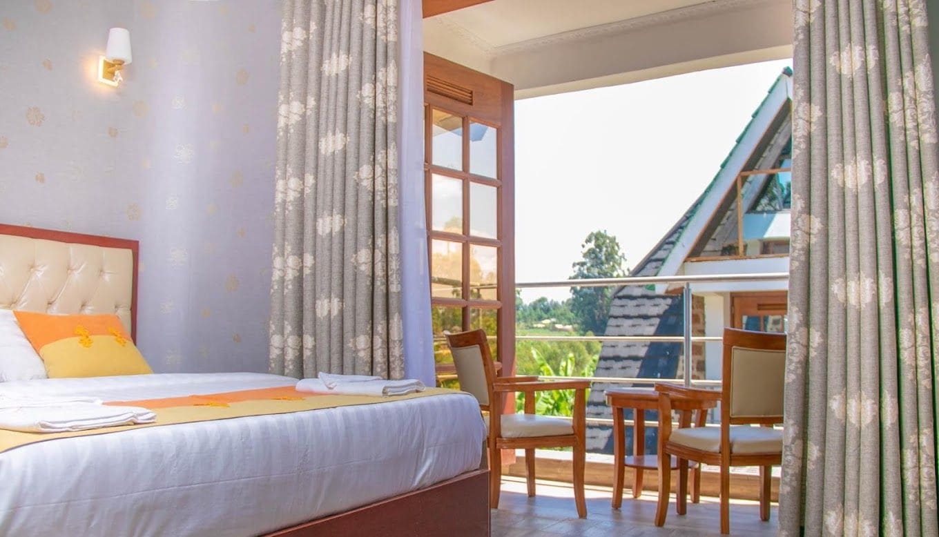 A bedroom with a large bed, a wooden headboard, and a view of a balcony with chairs.