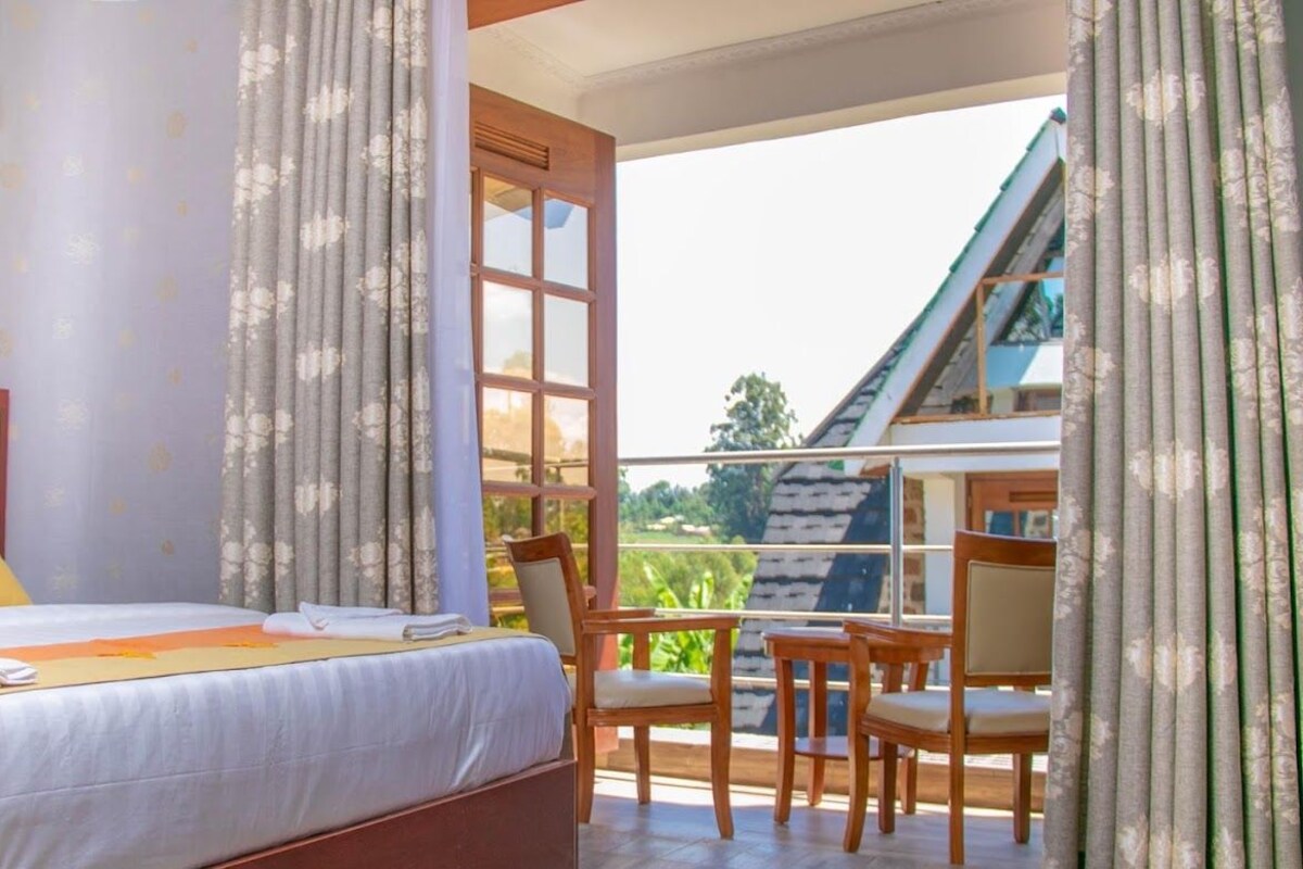A bedroom with a large bed, a wooden headboard, and a view of a balcony with chairs.