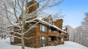 Una cabaña de madera con un amplio porche y numerosas ventanas, rodeada de árboles cubiertos de nieve.