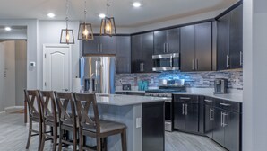 A modern kitchen with dark cabinets, stainless steel appliances, and a central island with chairs. - Peaceful Location w/Sunset & Wildlife Views, Htd Pool, Hot Tub, Fire Table, 2 Bikes (Gold Canyon)