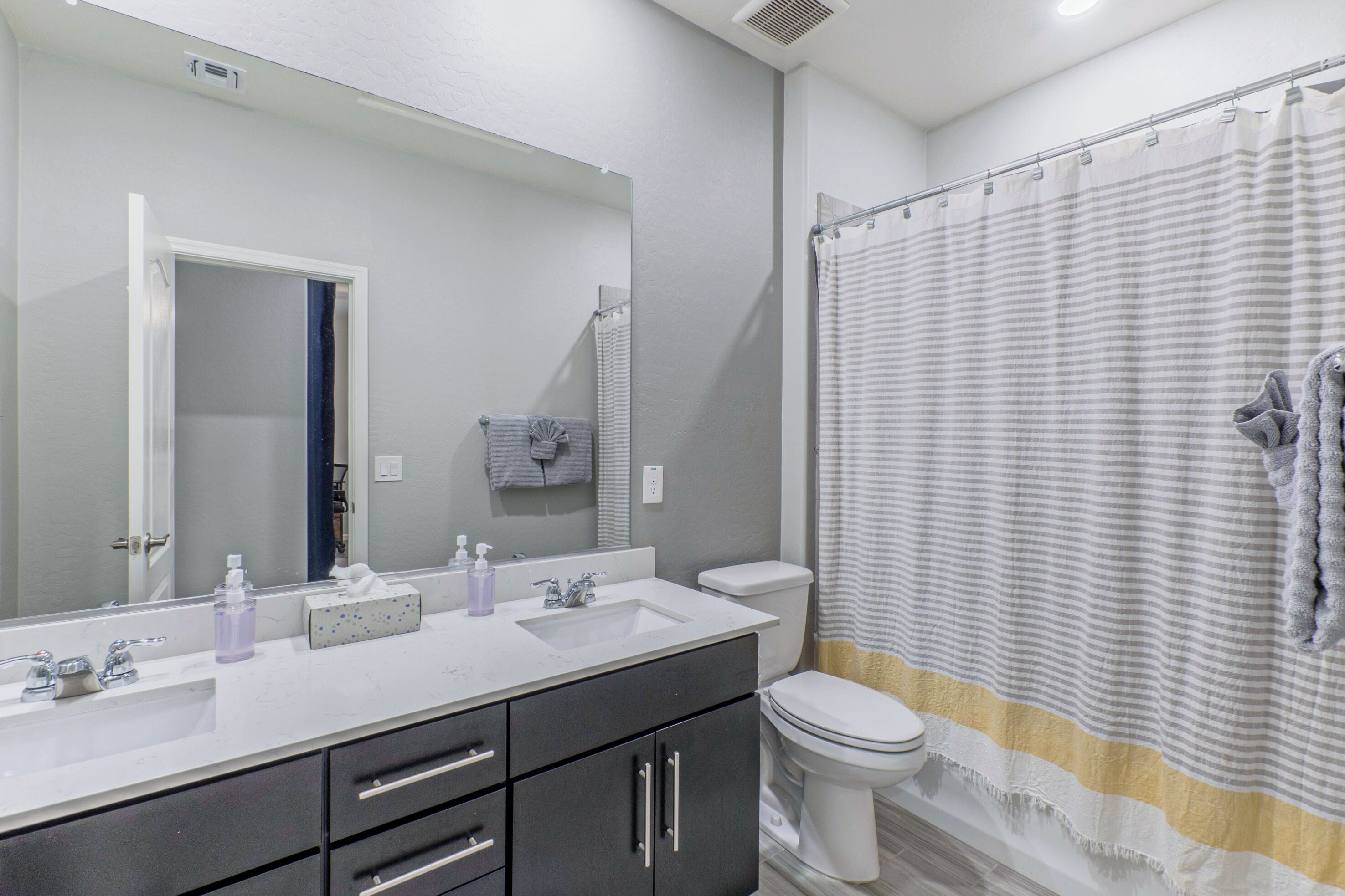A bathroom with a white sink, dark cabinets, a toilet, and a shower curtain.