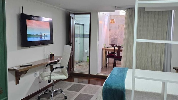A hotel room with a TV, a desk, a chair, a bed, and a view of the outside. - Amazônia Studio: experience the essence of the region (Belém)