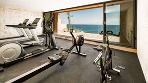 Un gimnasio con cintas de correr, elípticas y una bicicleta estática, con vista al océano a través de amplias ventanas.
