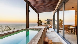 Piscina infinita moderna con vistas despejadas al océano, mobiliario de terraza de madera y un área de comedor con paredes de vidrio.
