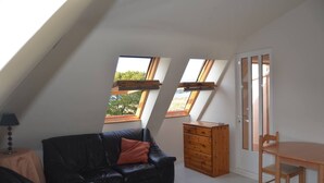 Un dormitorio tipo loft con techo inclinado, dos tragaluces, un sofá de cuero negro, un aparador de madera y una mesa de comedor con sillas.