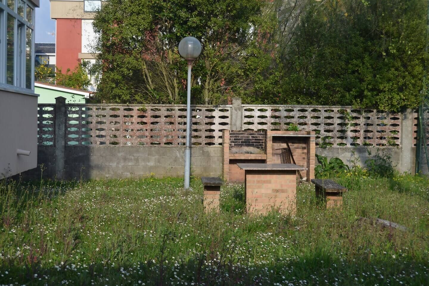 Un jardín con un farol de metal, un muro de ladrillo con diseño de celosía y una pequeña construcción de madera.