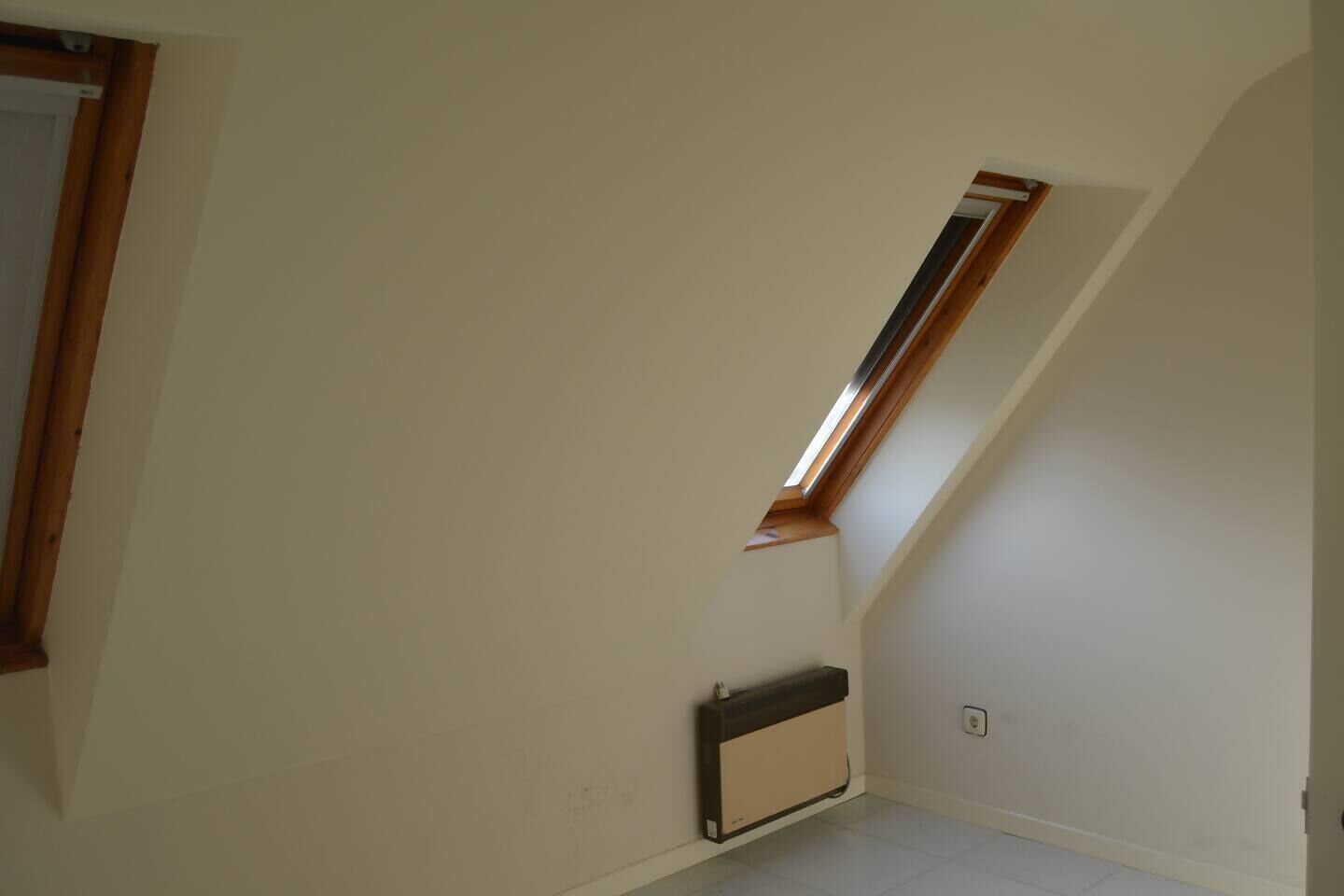 Una habitación con techo inclinado, tragaluz y radiador.