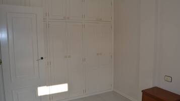 Una habitación con un armario blanco grande, una mesita de noche de madera y suelo de baldosas.