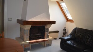 Una habitación con chimenea de piedra, un sofá de cuero negro y un tragaluz.