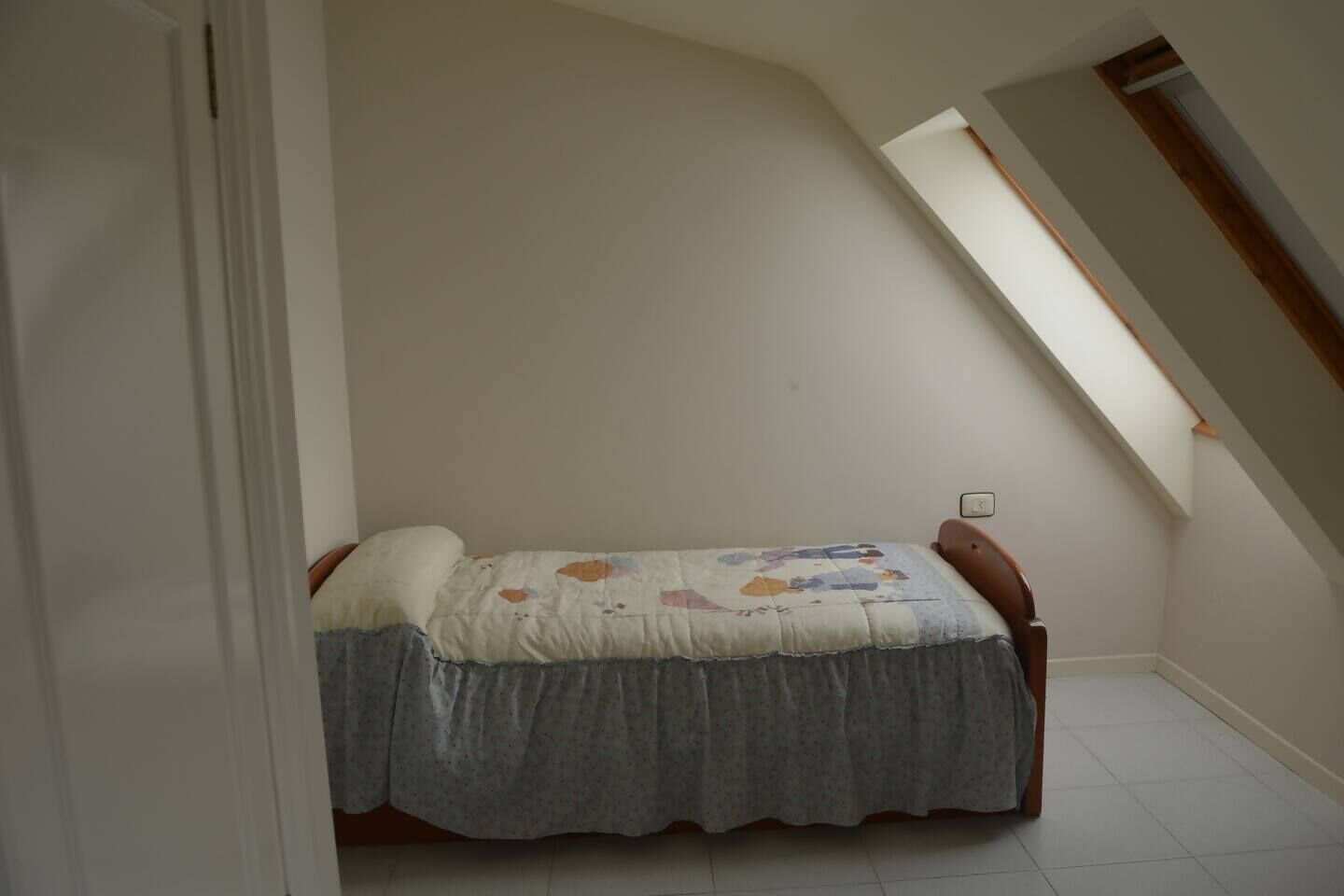 Una habitación pequeña con cama individual, techo inclinado y tragaluz.