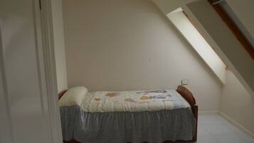 Una habitación pequeña con cama individual, techo inclinado y tragaluz.