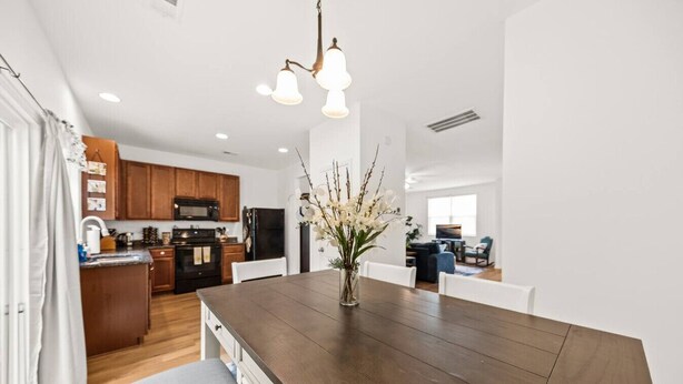 A modern kitchen with wooden cabinets, a central island, and a dining area with a dark wooden table and white chairs. - Southern Oak Cottage (Ladson)