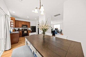 A modern kitchen with wooden cabinets, a central island, and a dining area with a dark wooden table and white chairs. - Southern Oak Cottage (Ladson)