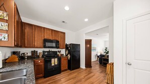 A kitchen with wooden cabinets, a microwave, a refrigerator, granite countertops, and a stainless steel sink. - Southern Oak Cottage (Ladson)