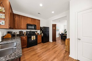 A kitchen with wooden cabinets, a microwave, a refrigerator, granite countertops, and a stainless steel sink.