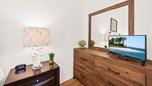 A wooden dresser with a television displaying a beach scene, a lamp, a clock, and a small plant. - Southern Oak Cottage (Ladson)