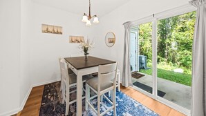 A dining area with a table, chairs, a chandelier, and a view of a garden through a sliding glass door. - Southern Oak Cottage (Ladson)