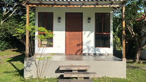 Ein kleines, eingeschossiges Haus mit einer gefliesten Veranda, einer Holztür und zwei Fenstern.