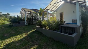 Ein modernes Haus mit überdachter Terrasse, einem kleinen Garten und Blick auf die umliegende Landschaft.