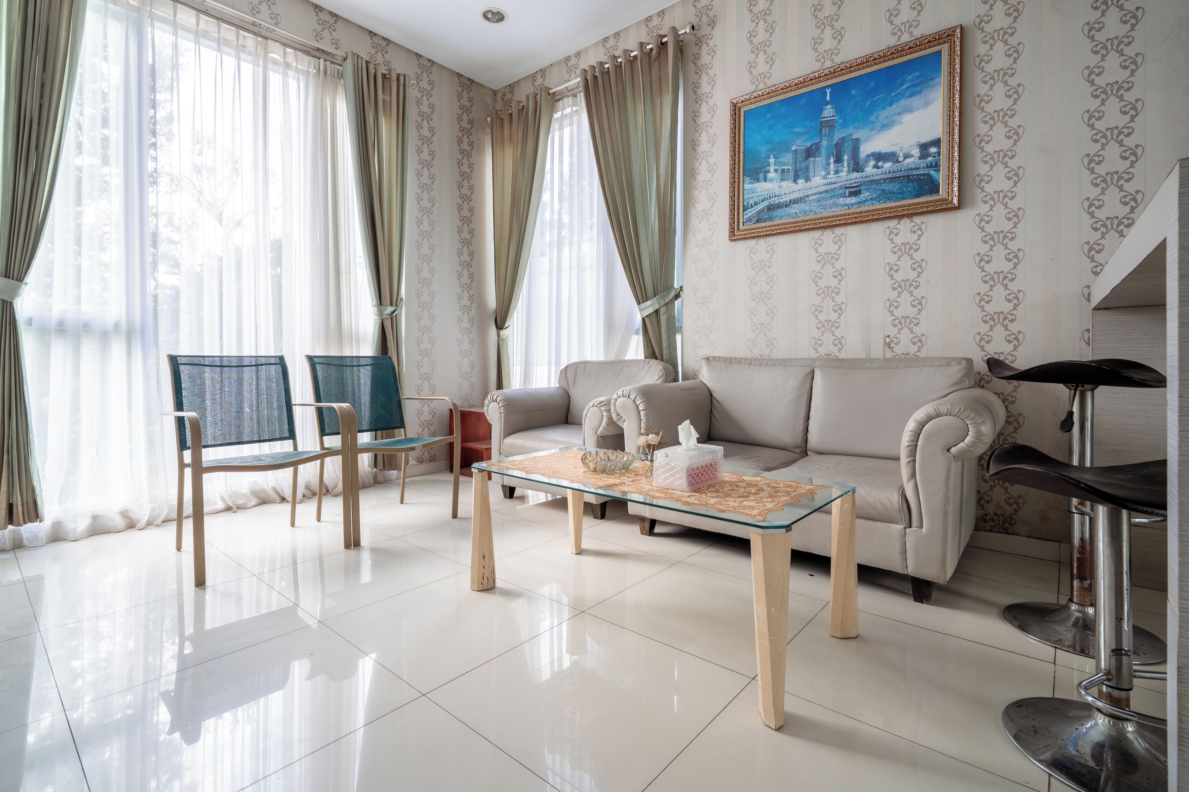 Una sala de estar con un sofá, dos sillones, una mesa de centro de vidrio y un cuadro en la pared.