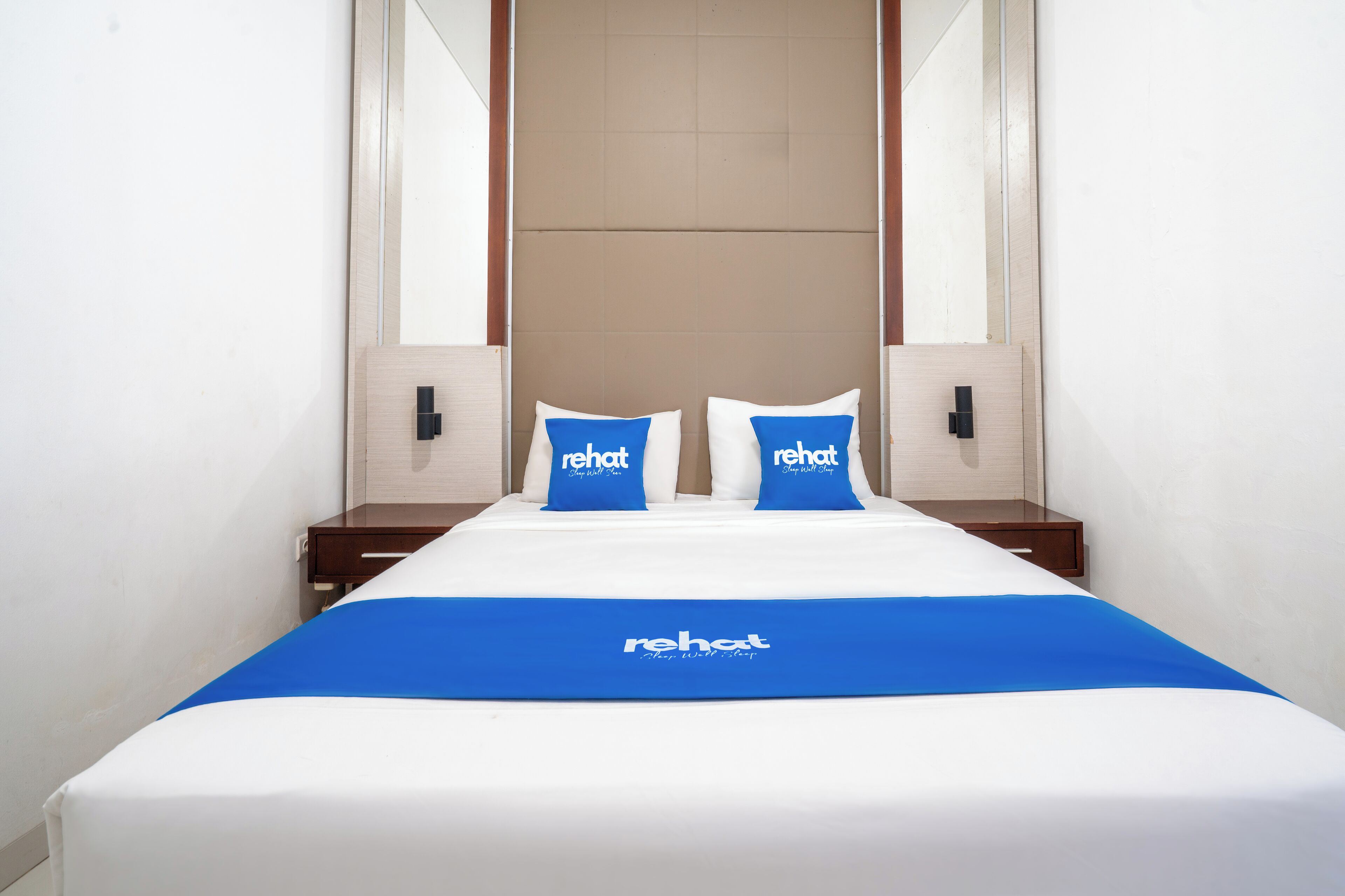 Une chambre d’hôtel avec un lit, deux tables de chevet et un grand miroir au-dessus du lit.