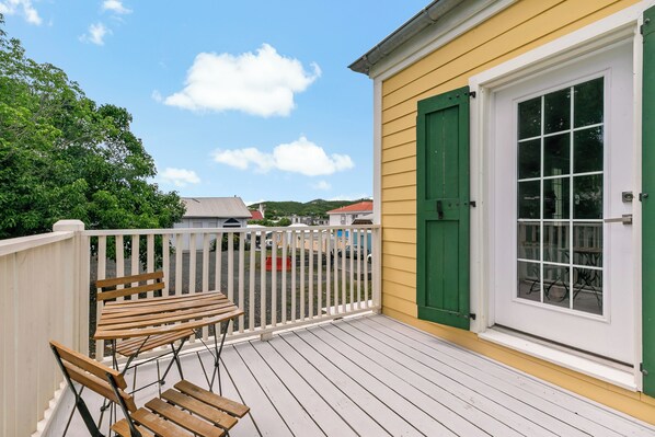 Une terrasse en bois avec deux chaises, une clôture blanche et un bâtiment jaune avec une porte et une fenêtre vertes.