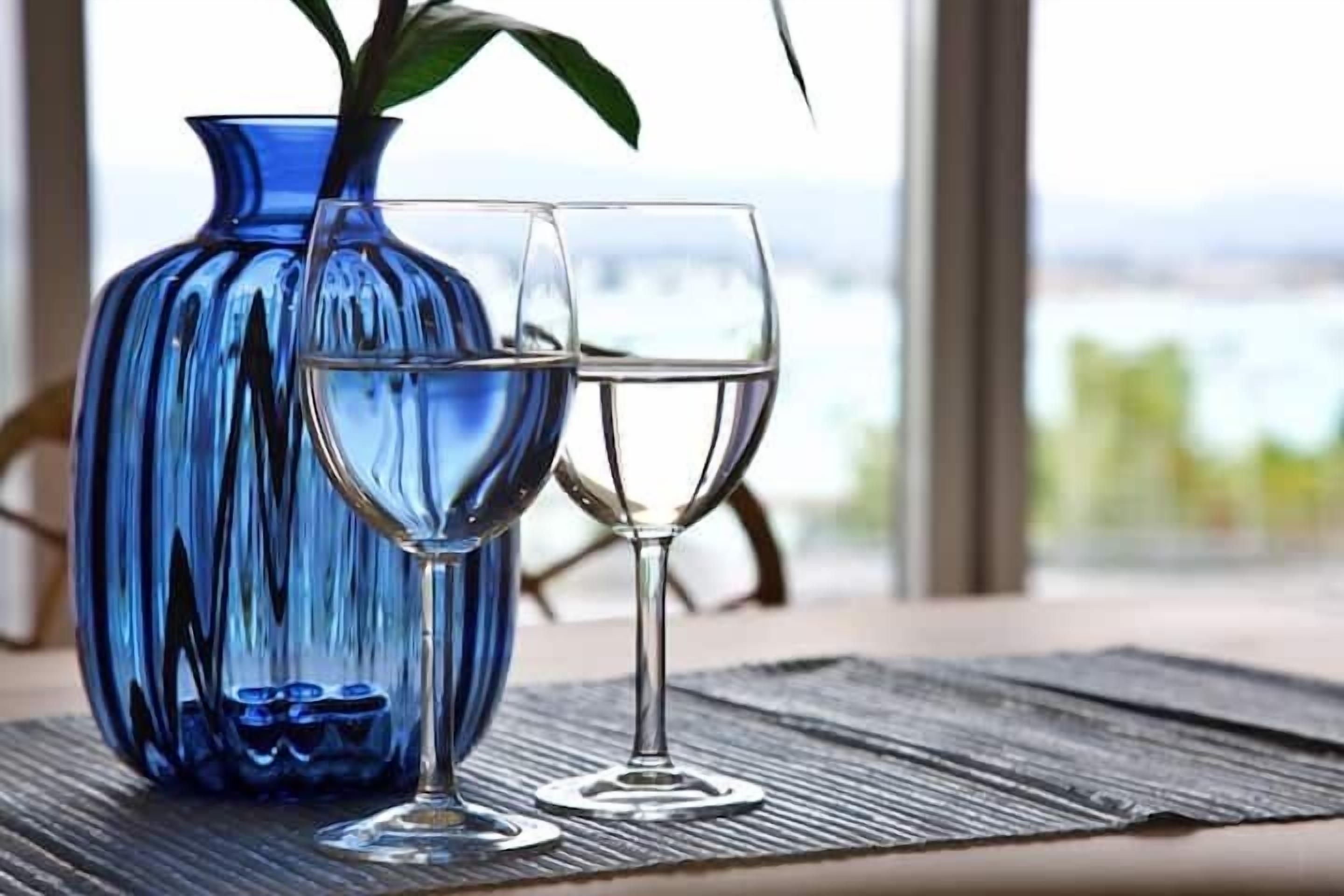 A blue vase with a plant on a table with two glasses of water.
