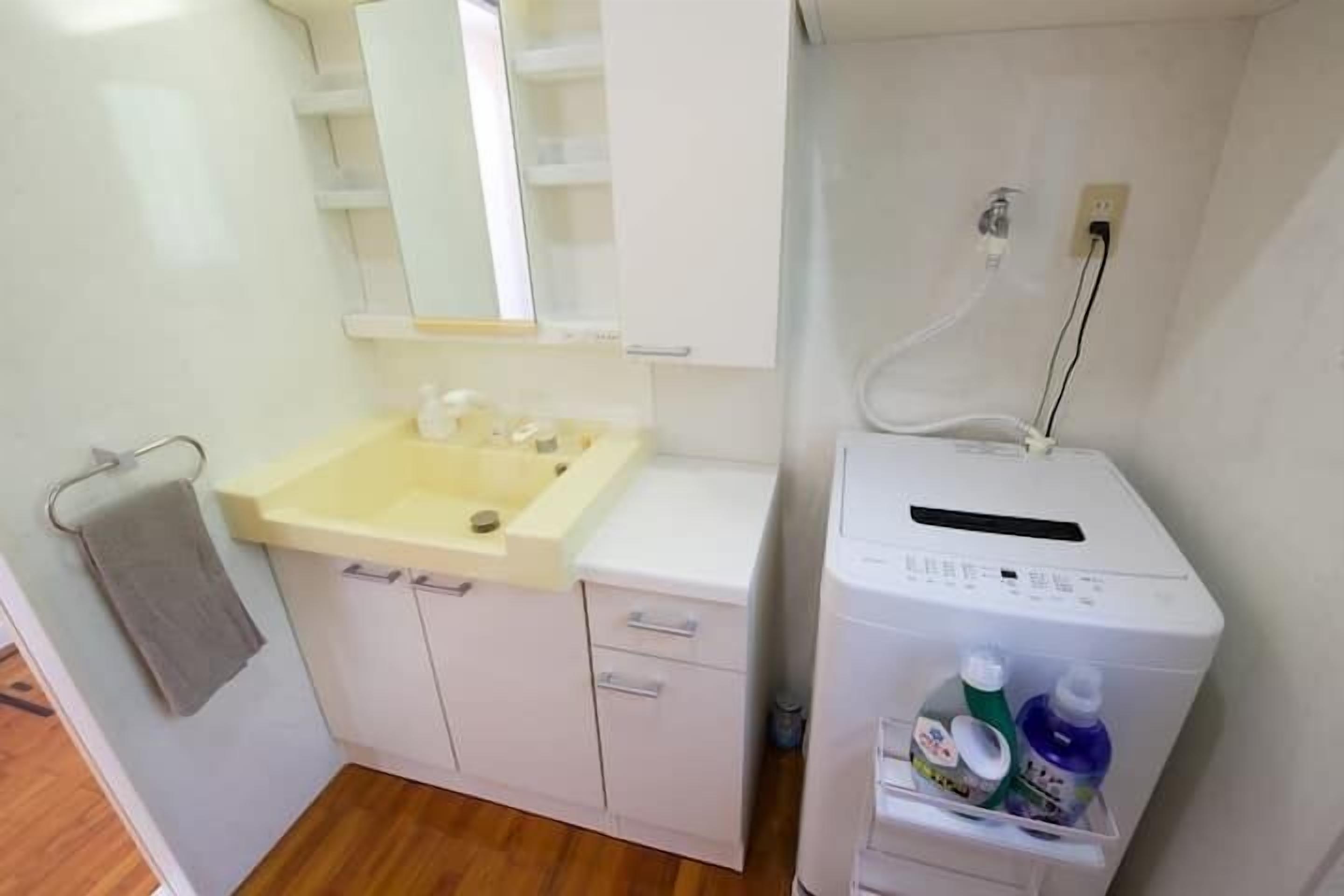 A small bathroom with a sink, mirror, cabinet, and a white washing machine.