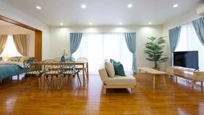 Ein geräumiges Wohnzimmer mit Holzboden, einer Couch, einem Fernseher und einem Essbereich mit Stühlen und einem Tisch.