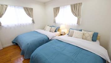 A hotel room with two beds, beige curtains, a wooden floor, and a nightstand with a lamp.
