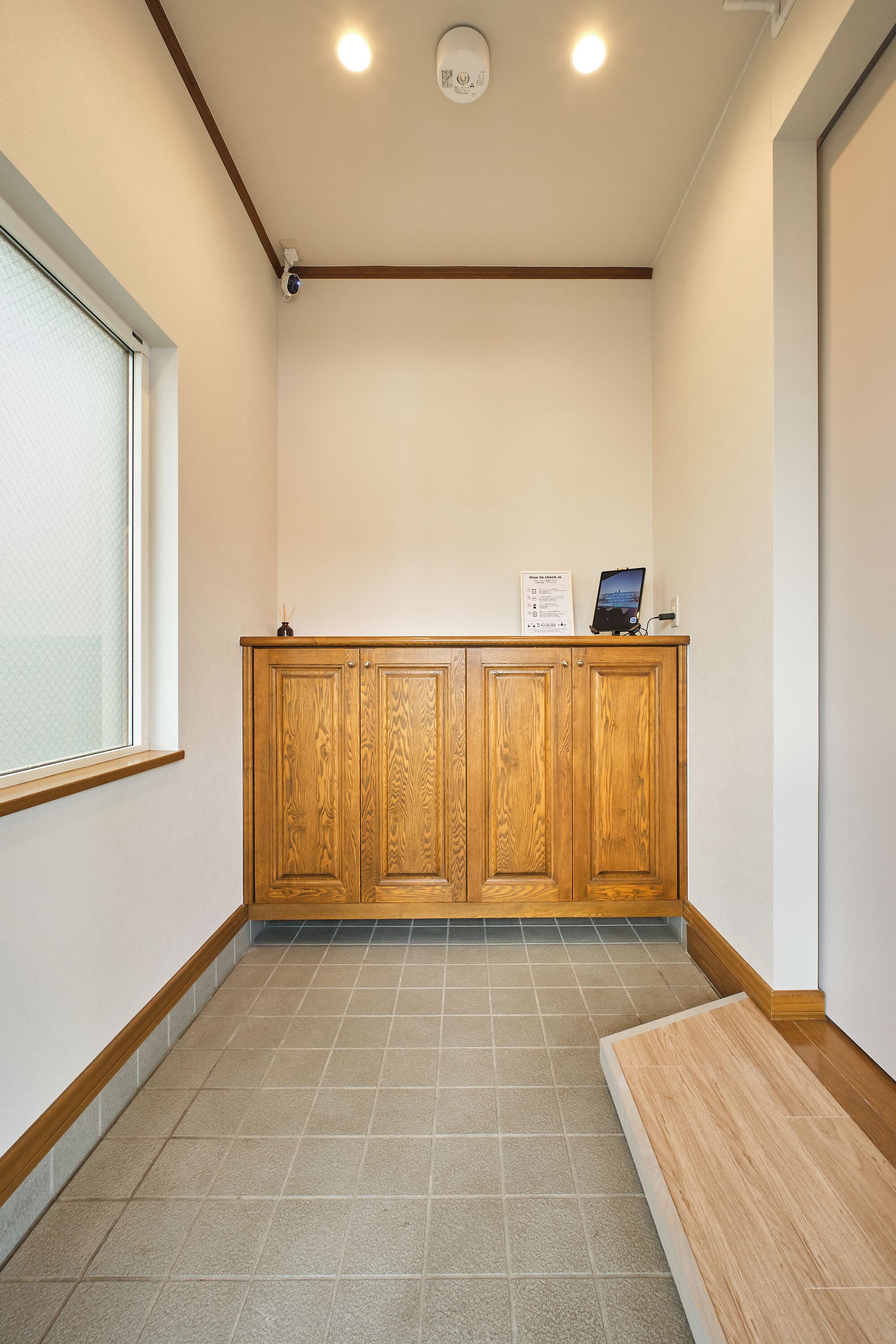 A hotel reception area with a wooden reception desk, a sign with check-in instructions, and a security camera.