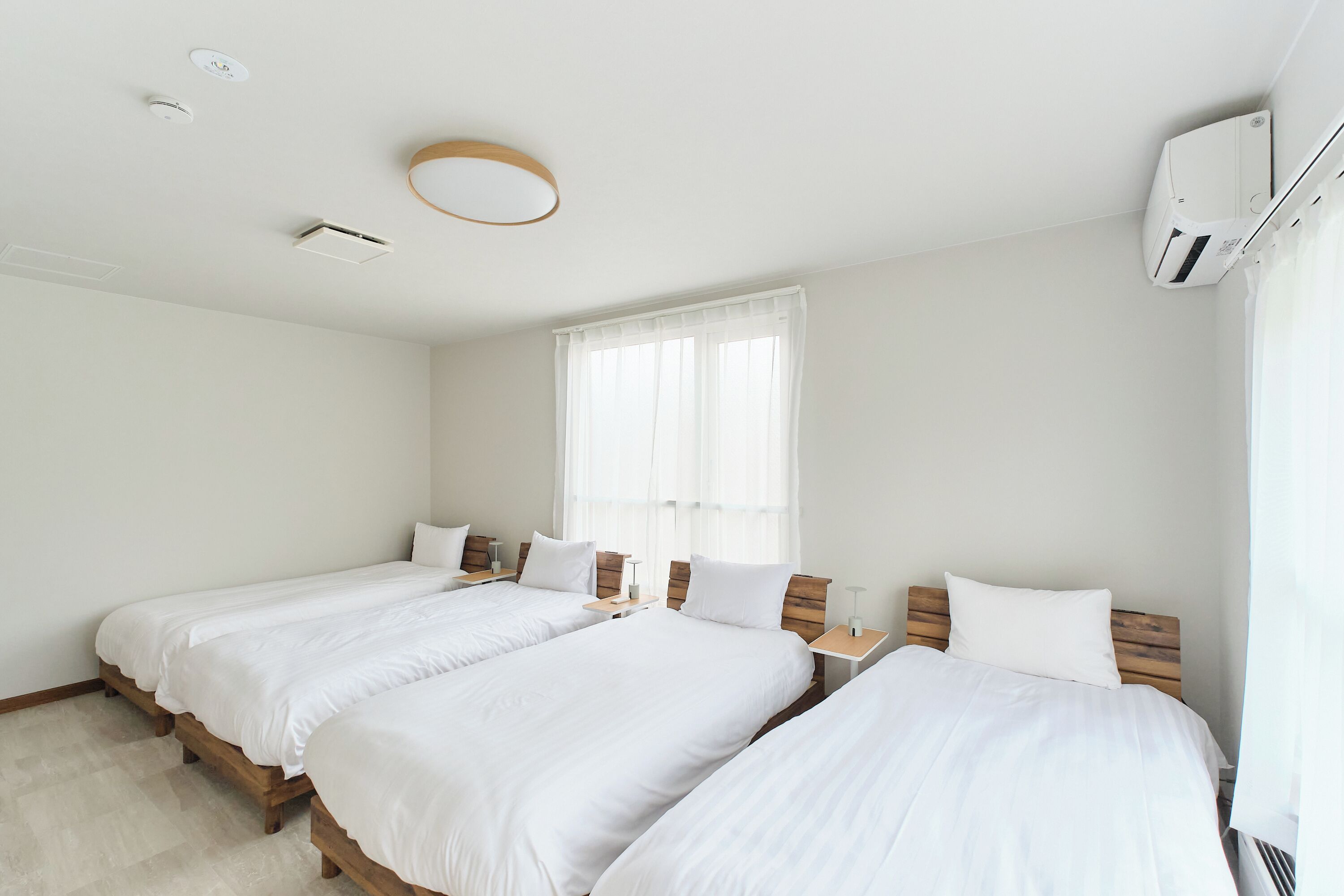 Ein Hotelzimmer mit zwei Einzelbetten, einem Fenster mit durchsichtigen Vorhängen, einem Deckenventilator und einer Klimaanlage.