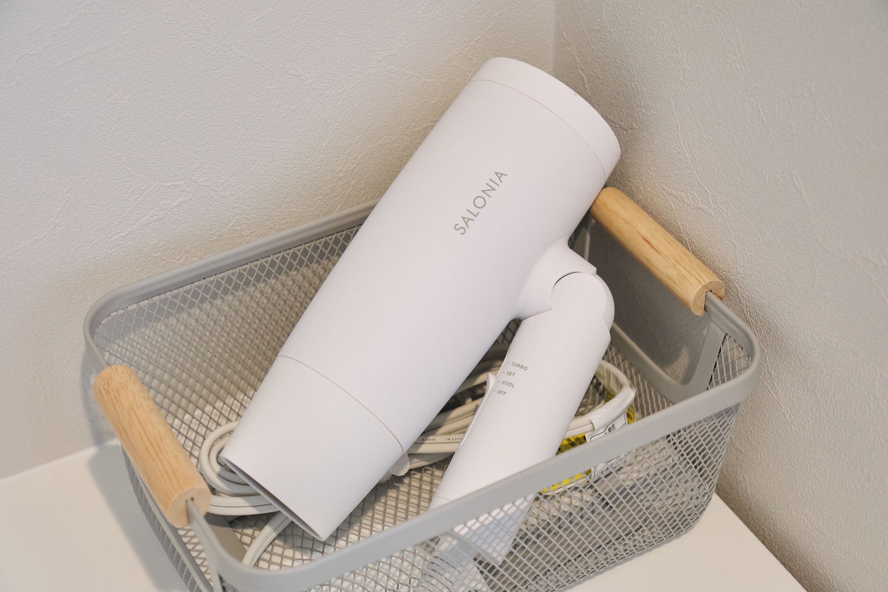 A gray wire basket containing a white hairdryer and a wooden-handled hairbrush.