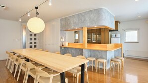 A modern kitchen with a wooden island, a dining area with a long table and chairs, and a hanging light fixture. - Hoshiyado Asahikawa asahimachi (Asahikawa)