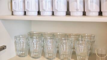 Una estantería con tazas blancas y vasos de vidrio transparentes.