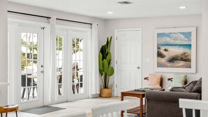 A room with a large window, a door, a plant, a painting, and a sofa.