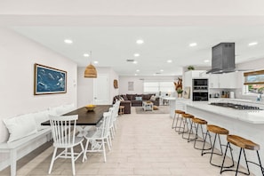 Una cucina moderna con mobili bianchi, un'isola centrale con sgabelli e luci a incasso nel soffitto.