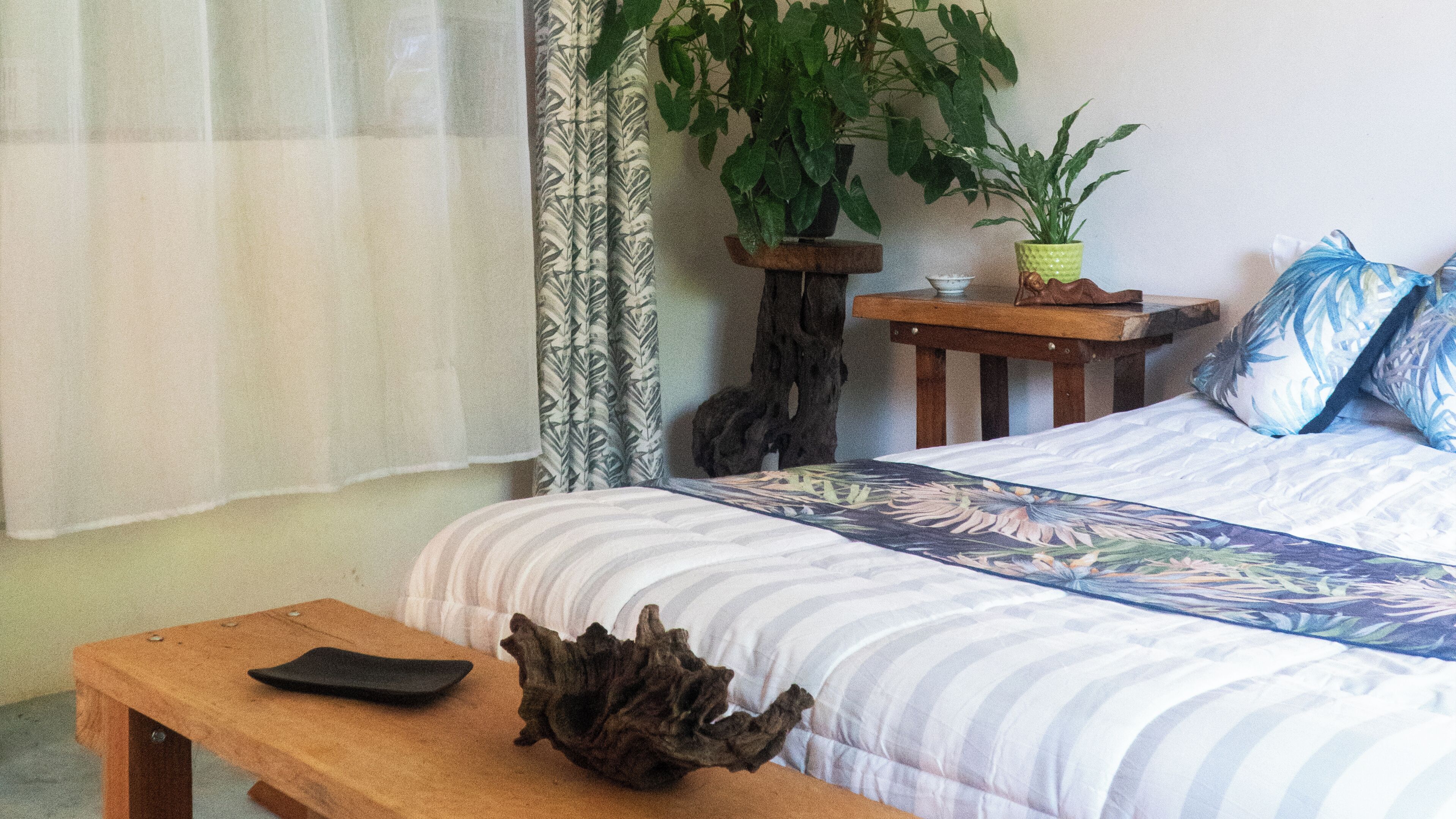 A bedroom with a bed, a wooden bench, a potted plant, and a small table.