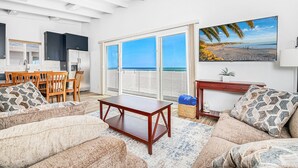A living room with a sofa, coffee table, and a painting of a beach. - Affordable 5BR Oceanfront Home with Pacific Views, Centrally Located between the Beach and the Bay! (Newport Beach)